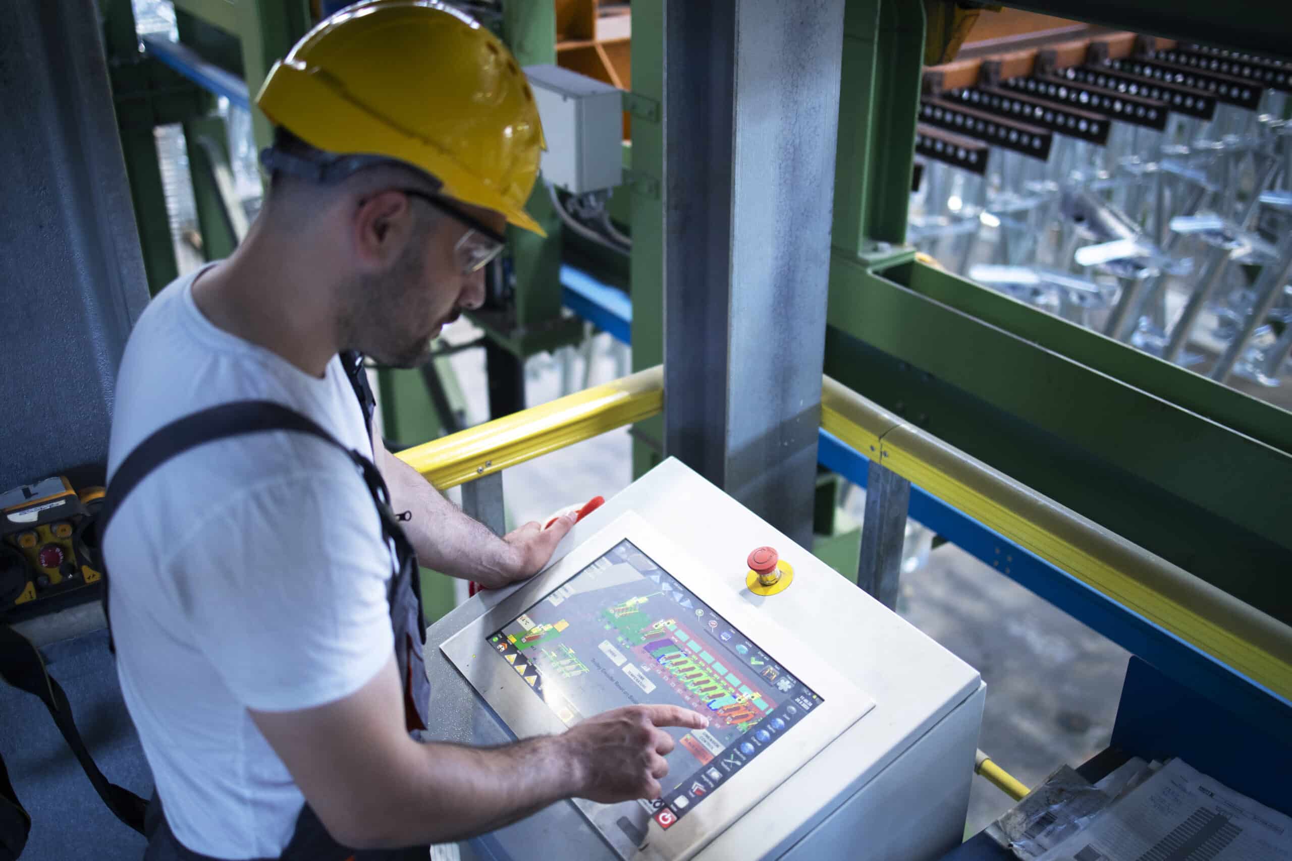 Operaio di fabbrica che monitora macchine industriali per la produzione da remoto in una sala di controllo su larga scala