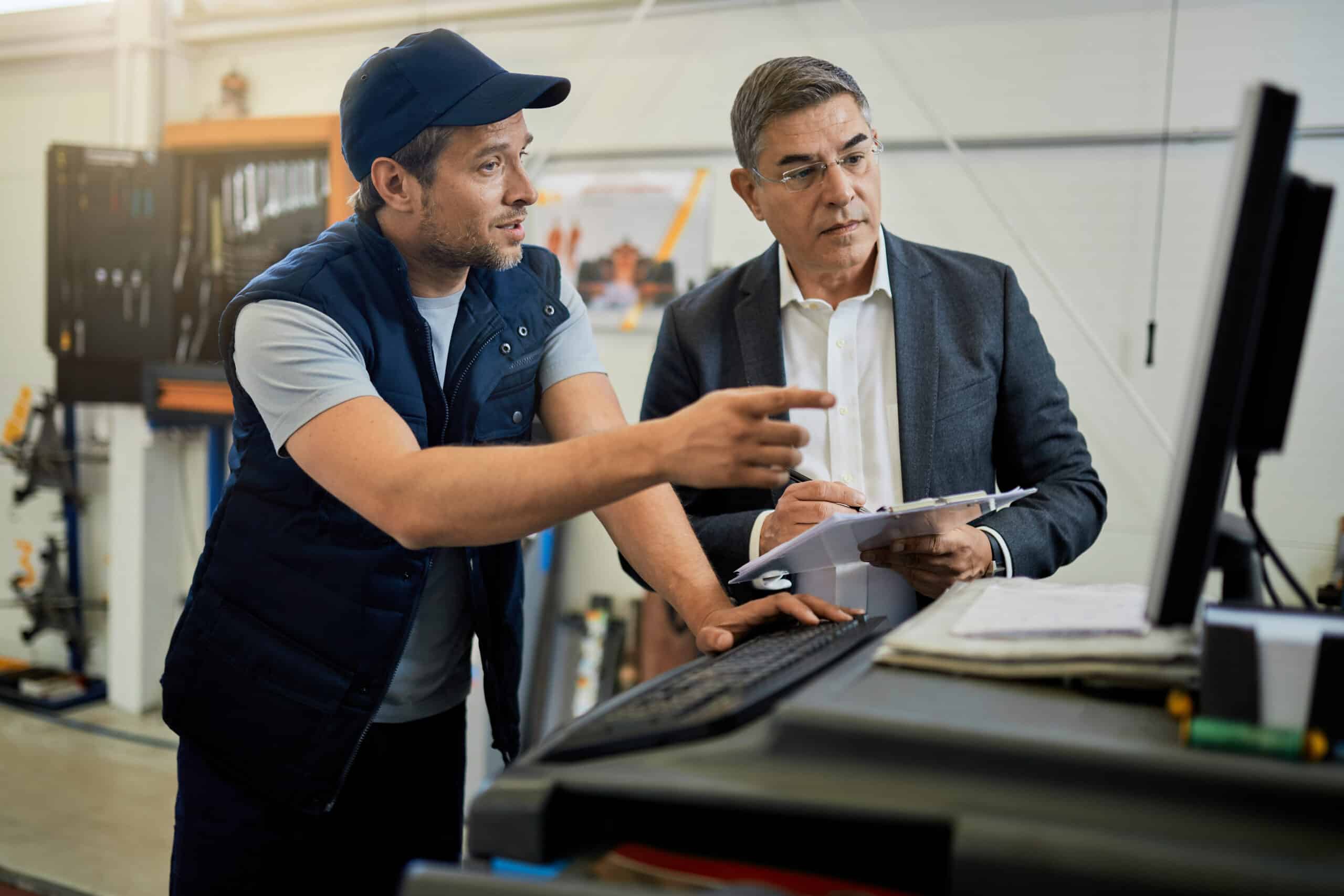 manager adulto medio meccanico automobilistico parla mentre usa il computer in officina