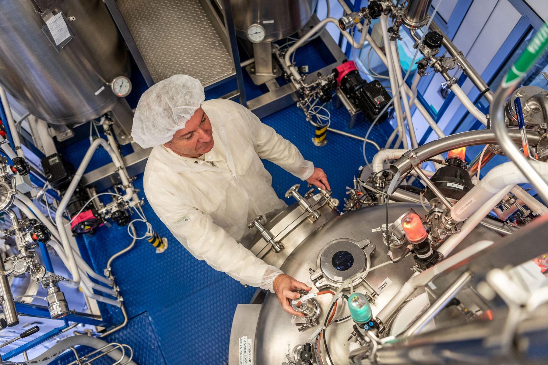 Operatore in camice e cuffia al lavoro su un reattore in acciaio nello stabilimento produttivo di Fidia Farmaceutici